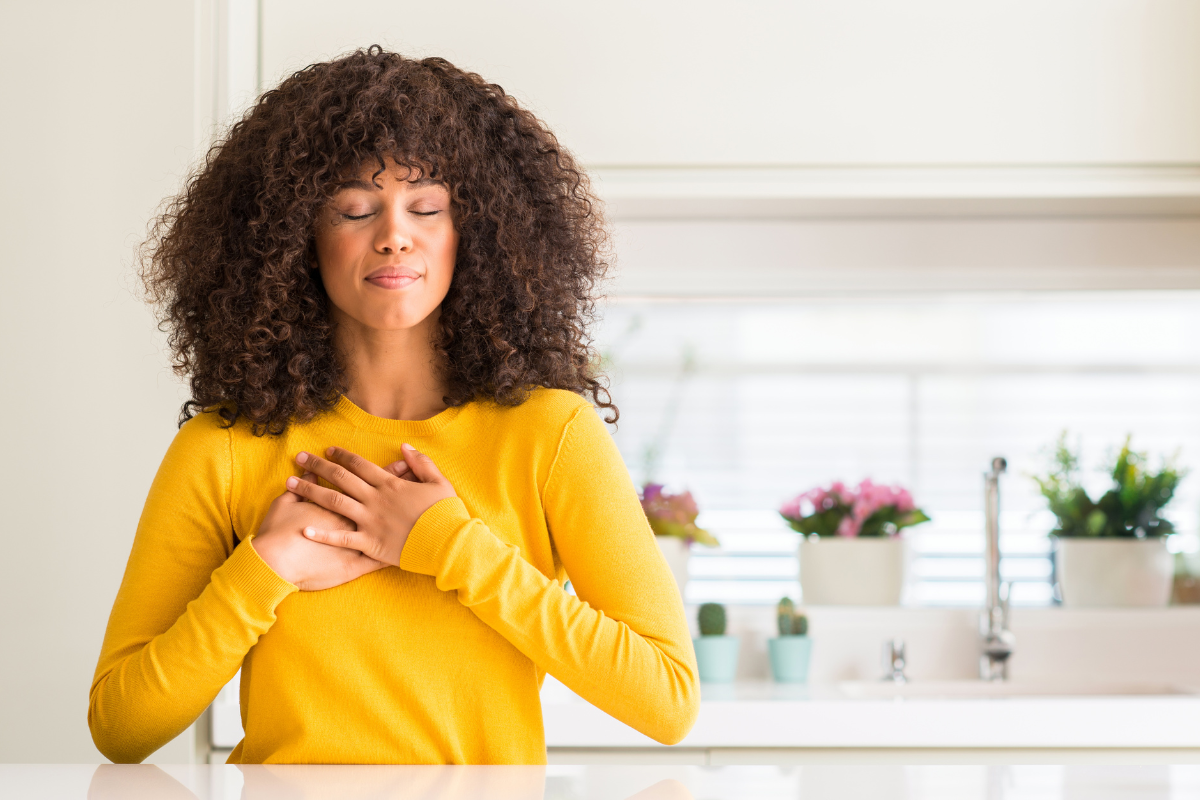 a woman wearing bright yellow holds her hands to her chest with her eyes closed seemingly enjoying a calm moment of gratitude