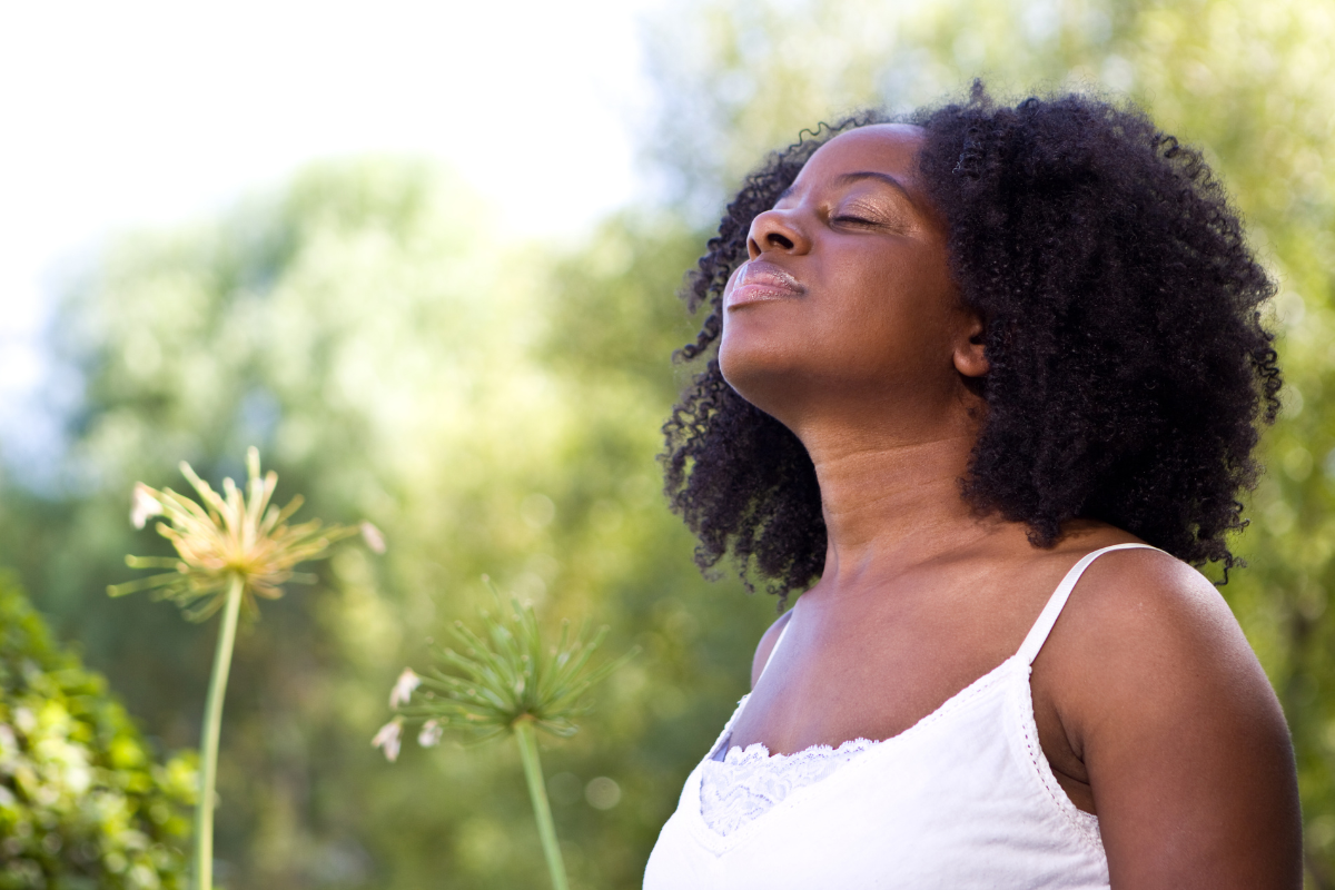 a woman stands outside with her head tilted toward the sun in a pose of gratitude