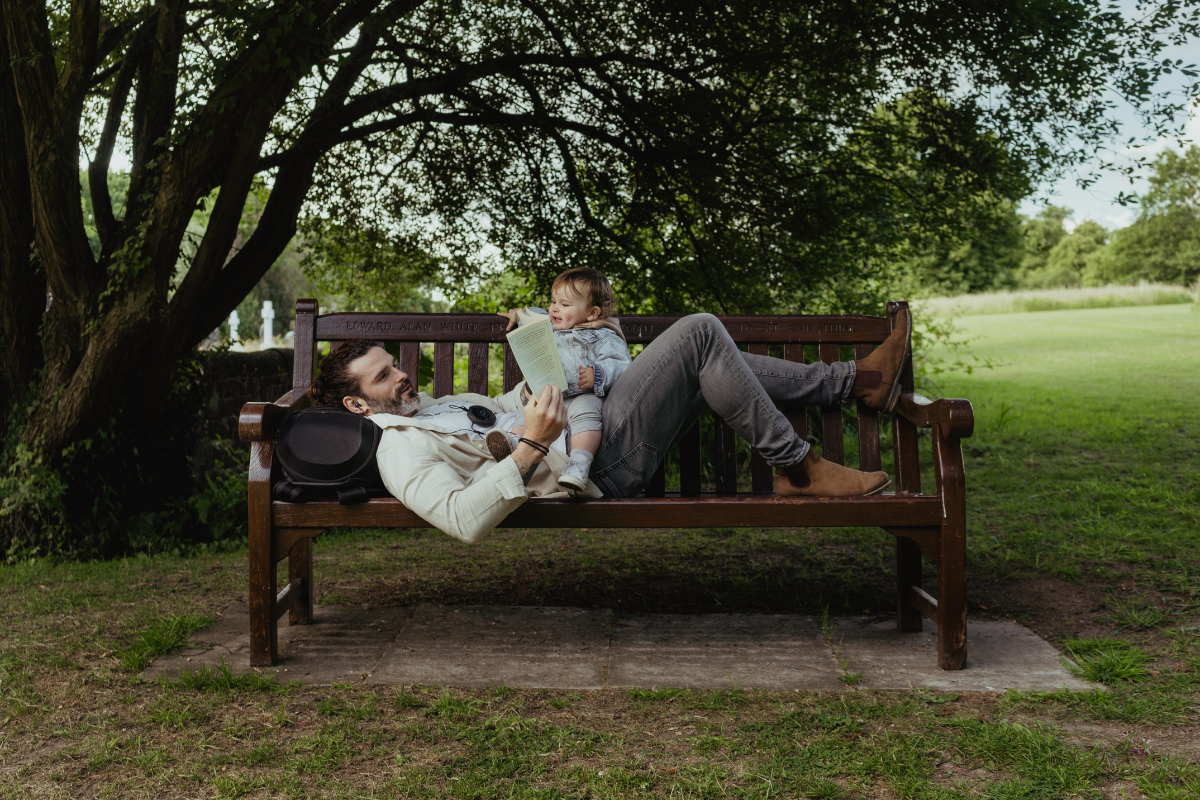 a man sits on a bench reading and using his Neuvana Xen while his baby distracts him
