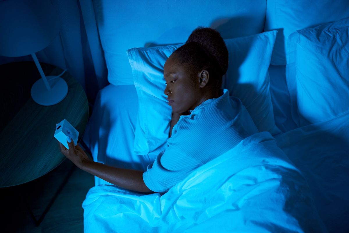 a woman lays in bed looking at the alarm clock