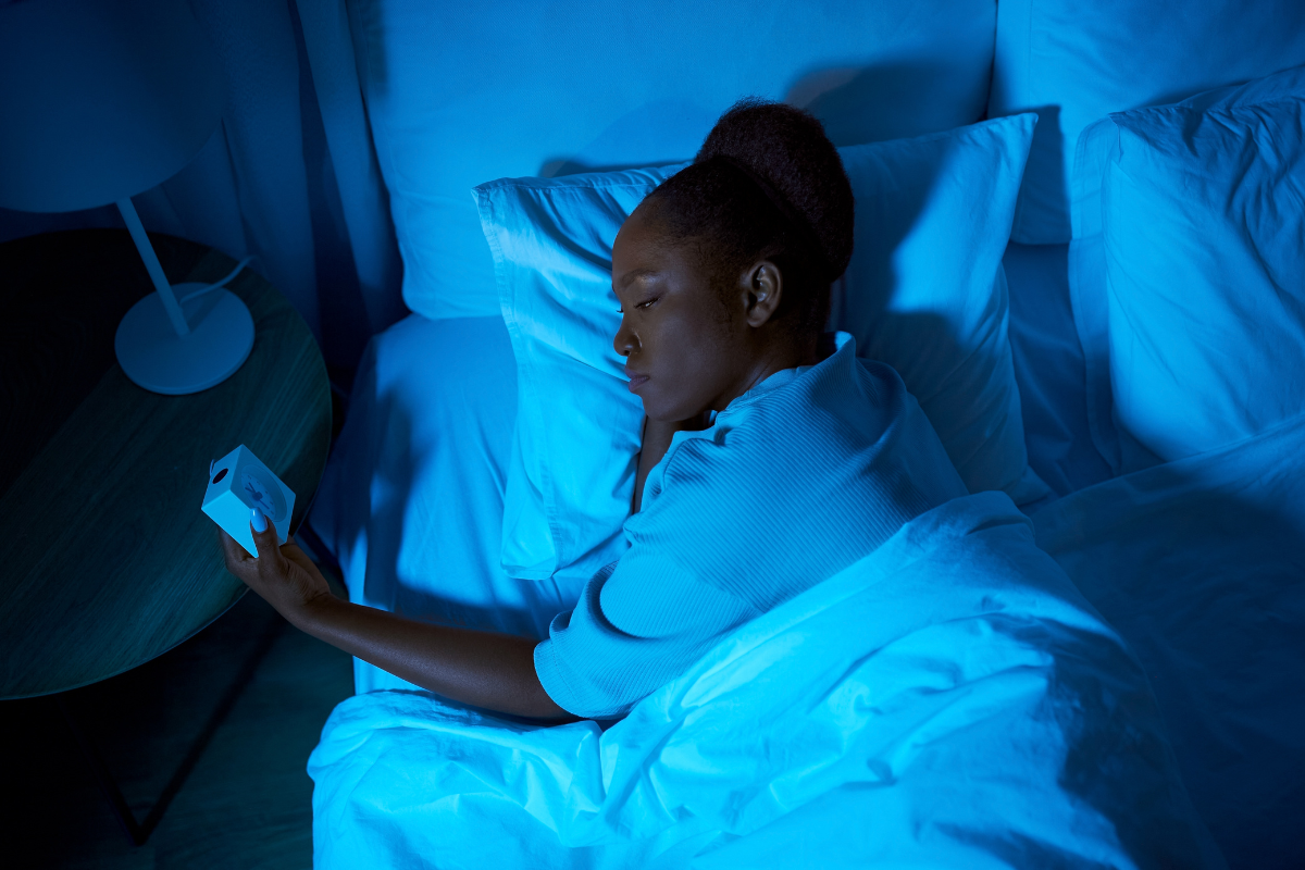 a woman lays in bed looking at the alarm clock 