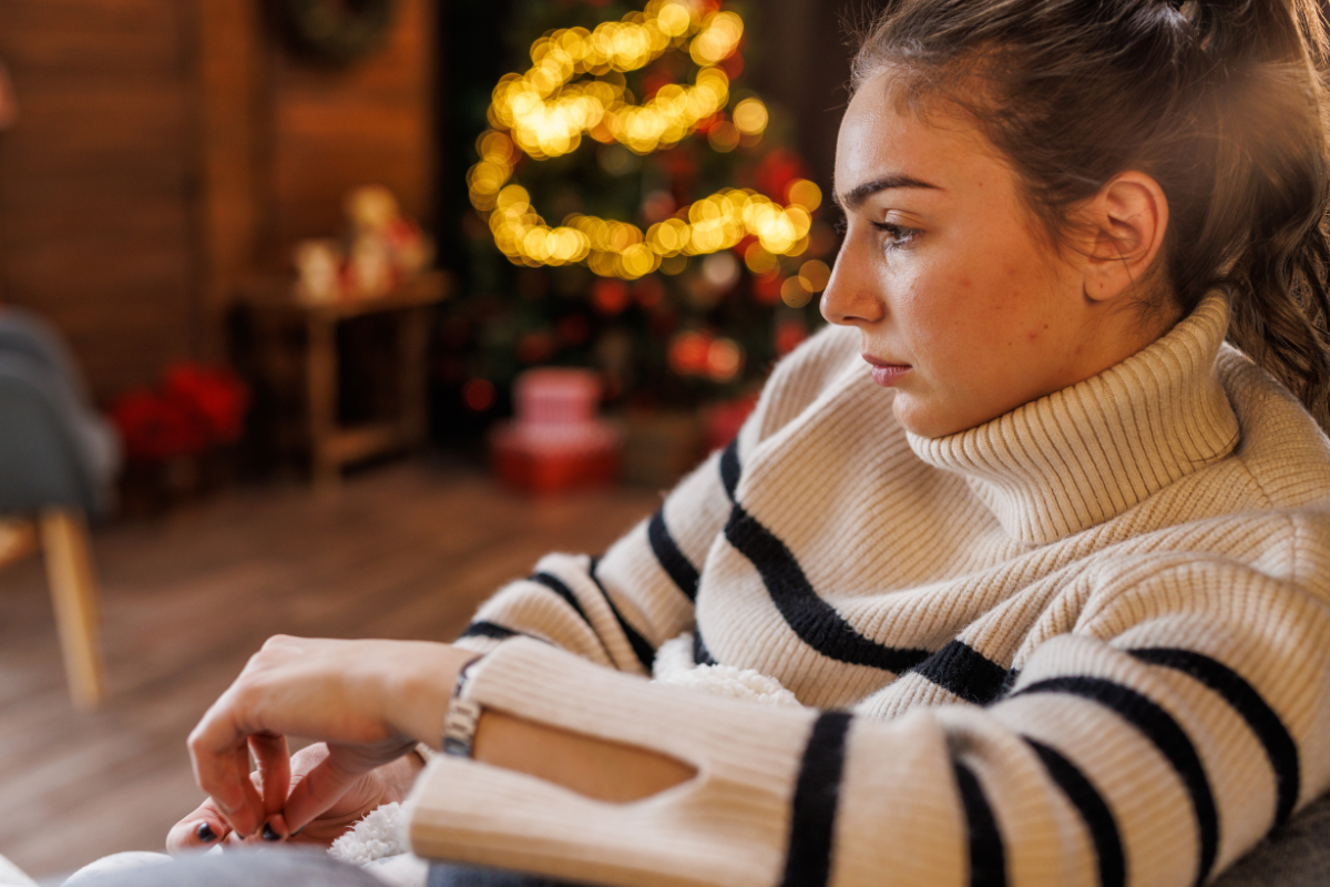 a woman sits alone with a sad expression near a christmas tree