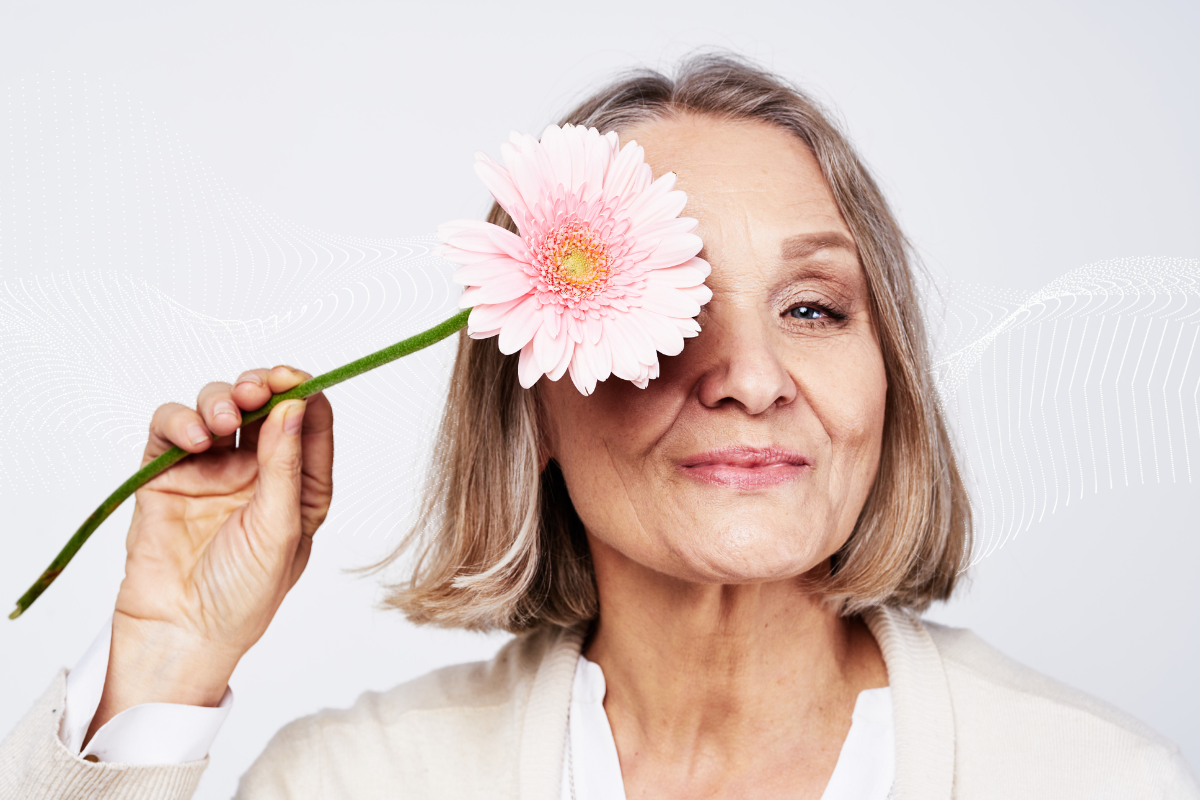 an older woman holds a pink flower covering her left eye
