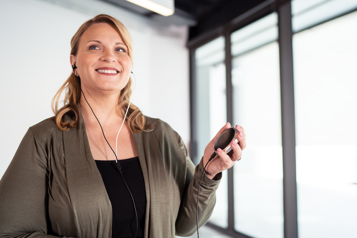 woman with blonde hair smiles at something off camera while holding a consumer vagus nerve stimulator called Xen by neuvana