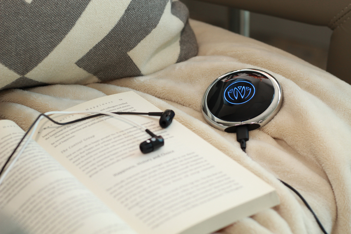 Neuvana's consumer vagus nerve stimulator lit up blue sitting on a blanket with a book next to it