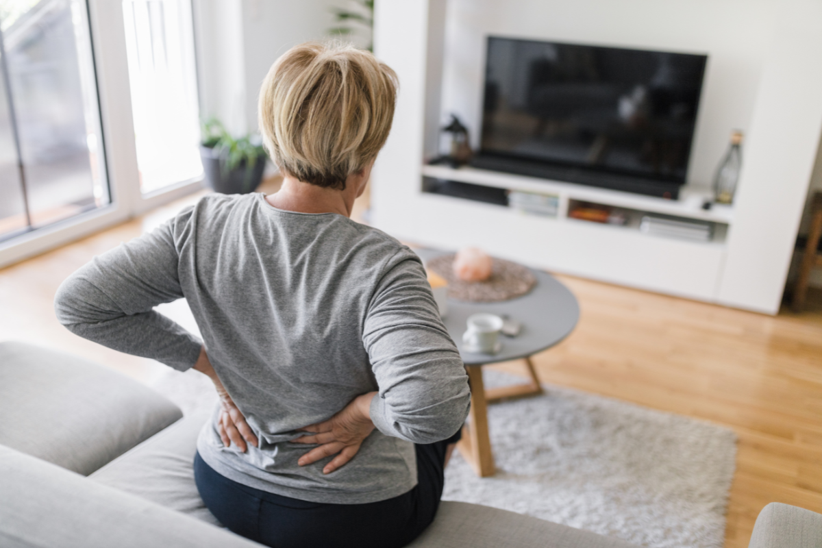 a woman sits on a couch clutching her lower back in pain