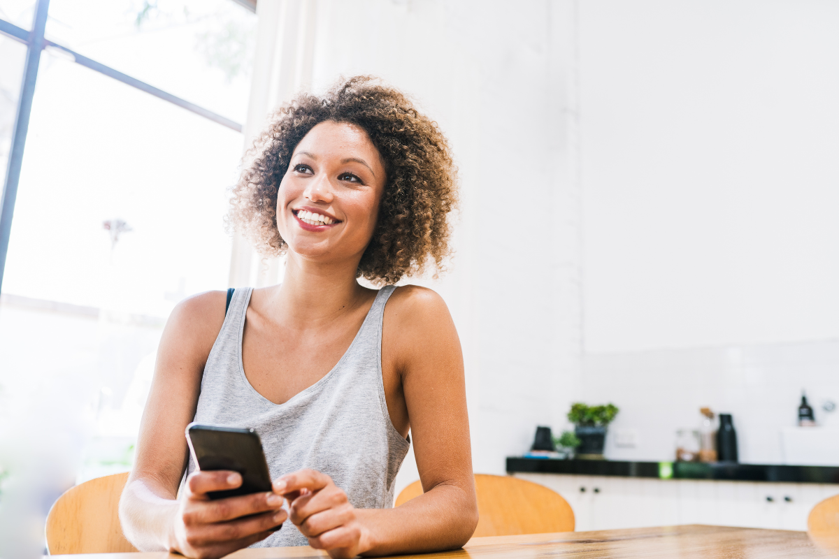 a woman sits at a table holding a phone looking optimistic