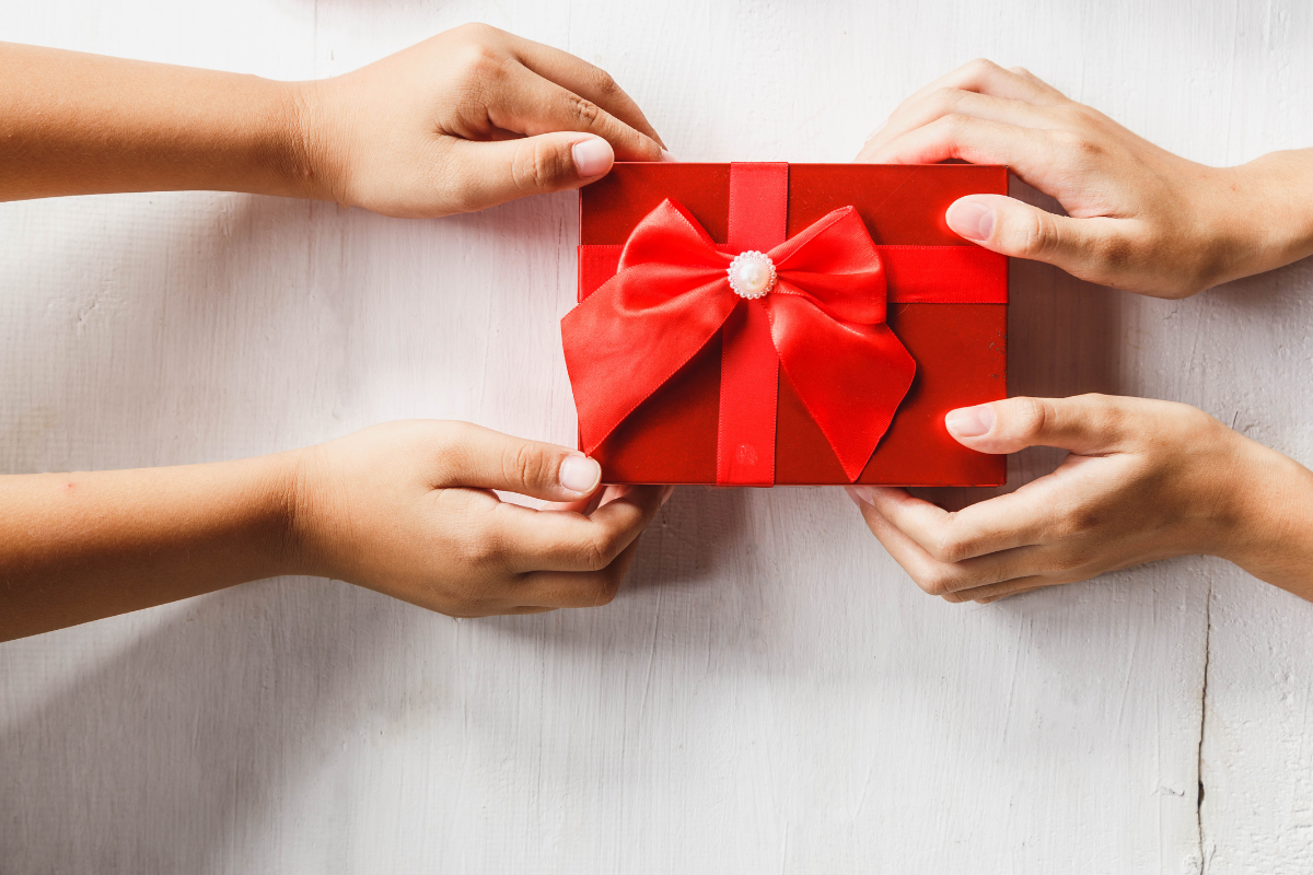 two sets of hands exchange a beautifully wrapped red giftbox with a red and white bow
