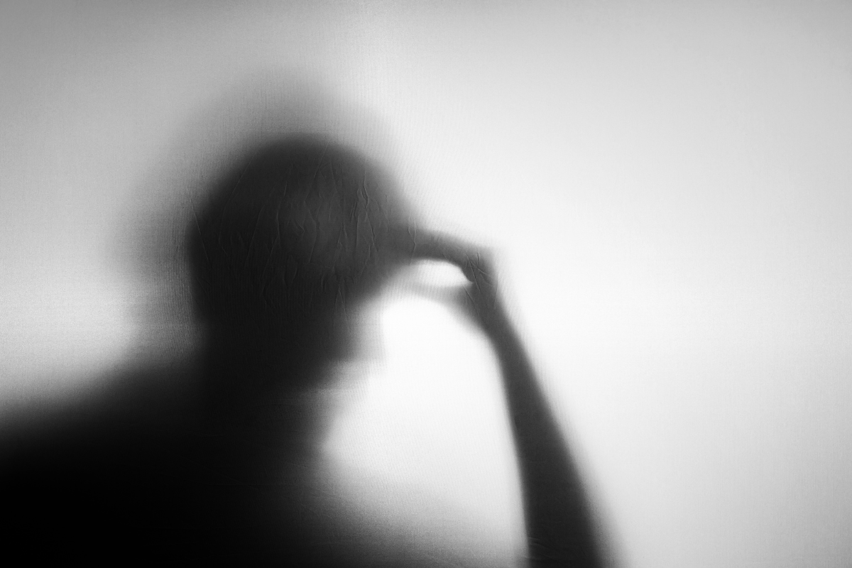 a silhouette of a sad person with a hand to their forehead in contemplation in shades of black white and grey 