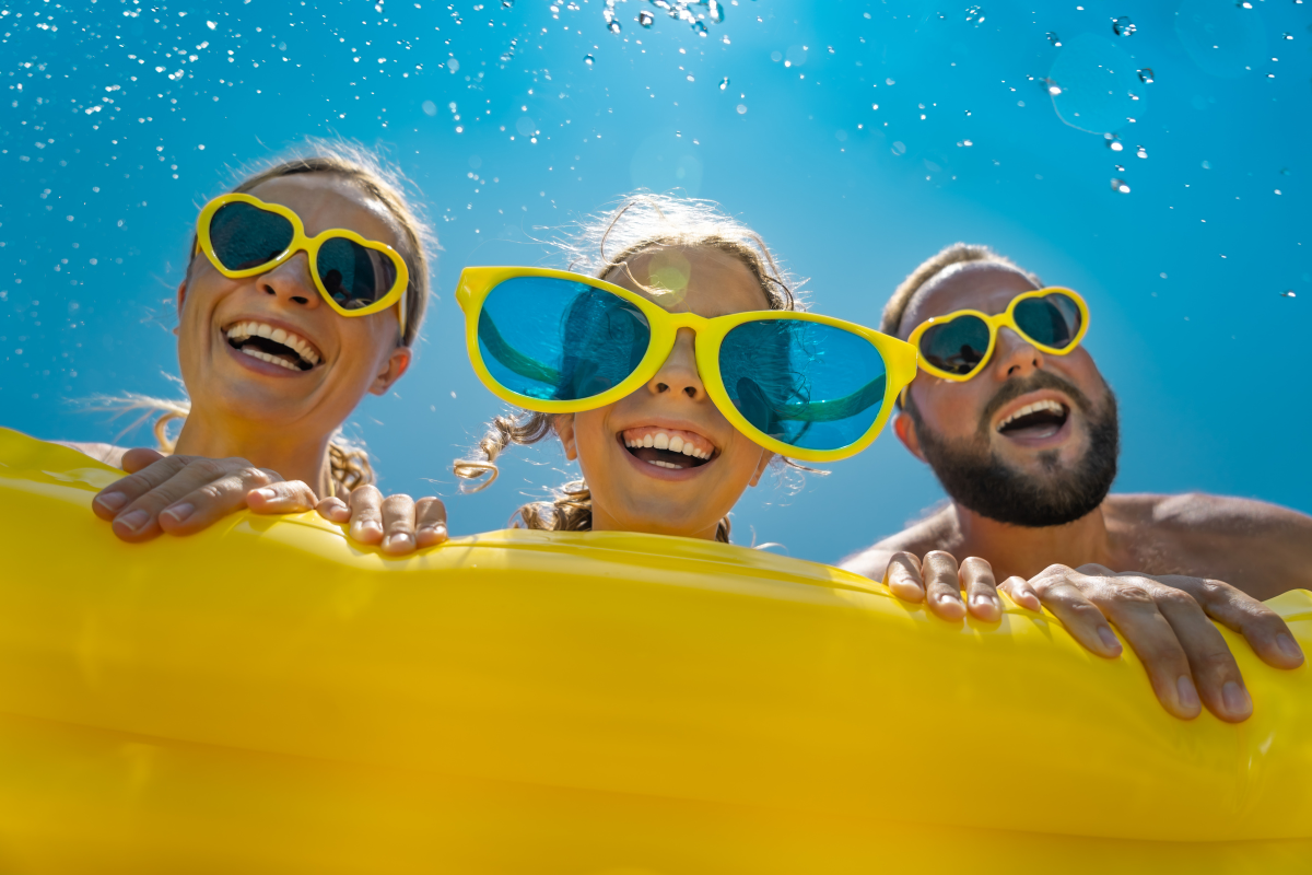 a mom, dad, and their child hold a neon yellow pool float and all are wearing matching yellow sunglasses