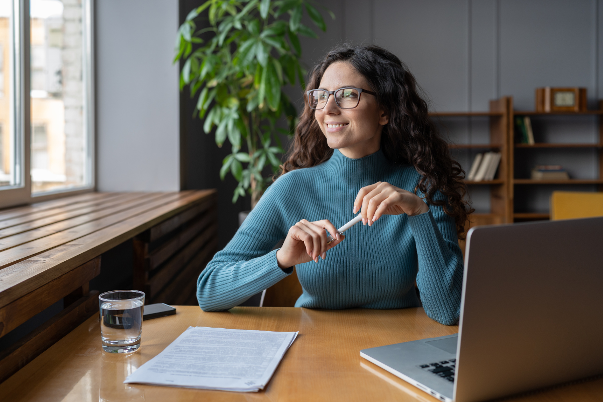 a woman sits at a desk looking out a window with a positive outlook