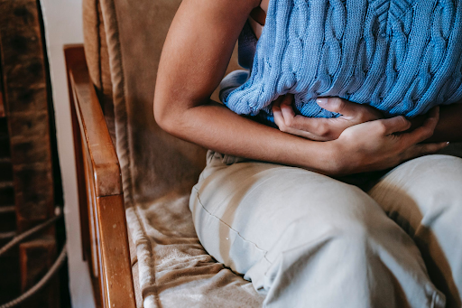 a person visible from the chest down is bent over at the waist clutching their stomach in what is clear gastric/digestive distress