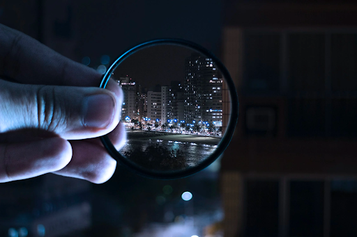a hand holds a lens that focuses in on a beautifully lit night skyline