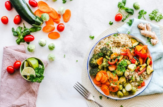 colorful summer vegetables like cherry tomatoes, zucchini, and carrots cover a white tablescape