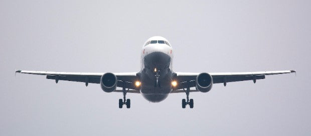 Grey commercial plane flying head on through a light grey sky