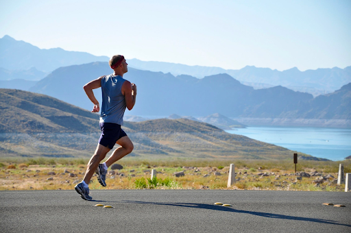 young man running on a road that is surrounded by a scenic mountain view