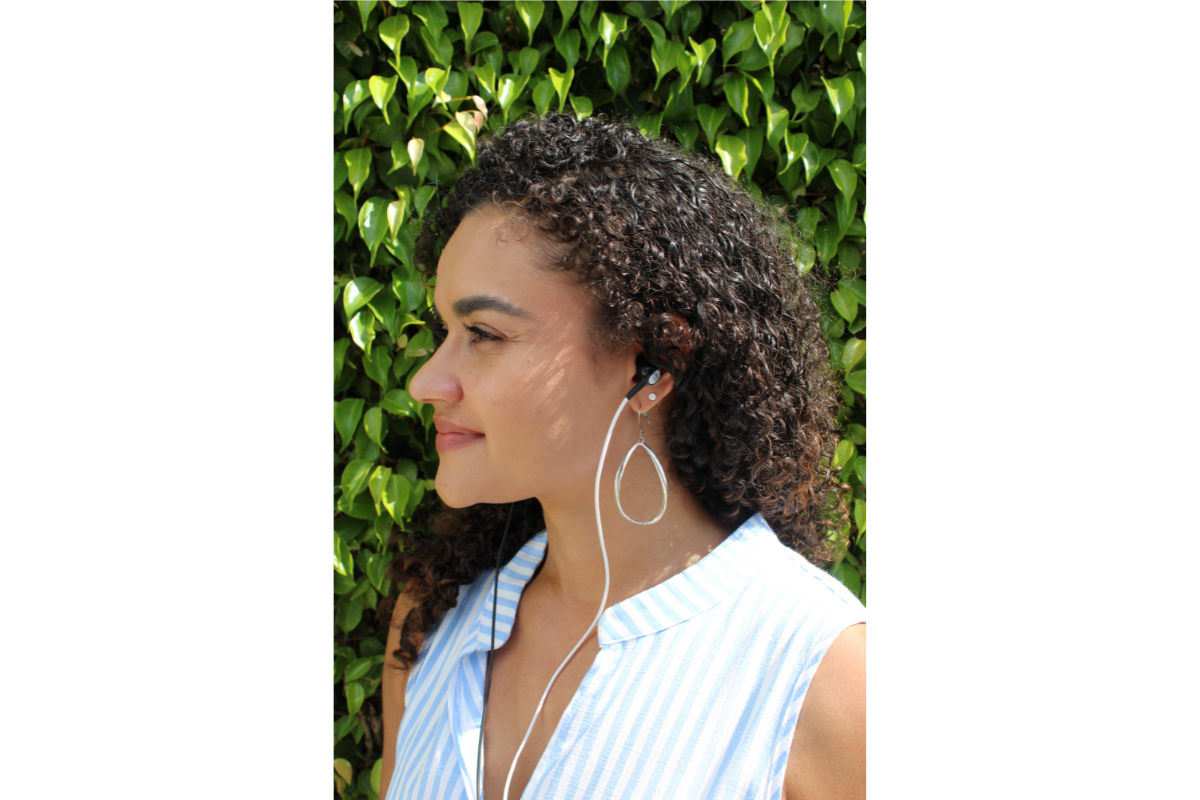 A woman with curly hair wearing earphones and a striped sleeveless shirt, standing in front of a leafy green background, with the Neuvana logo at the bottom