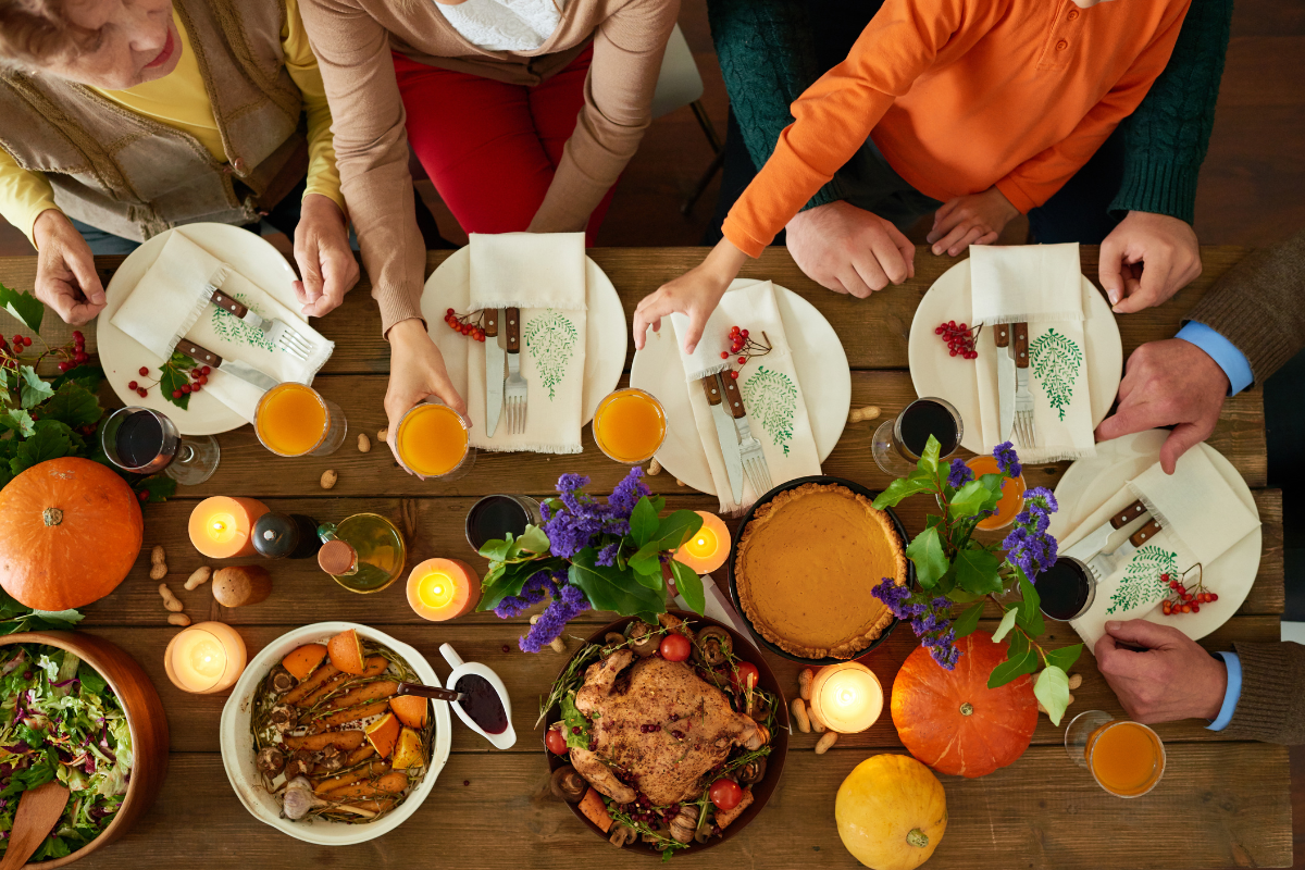 birds eye view of a festive thanksgiving table with hands reaching for food