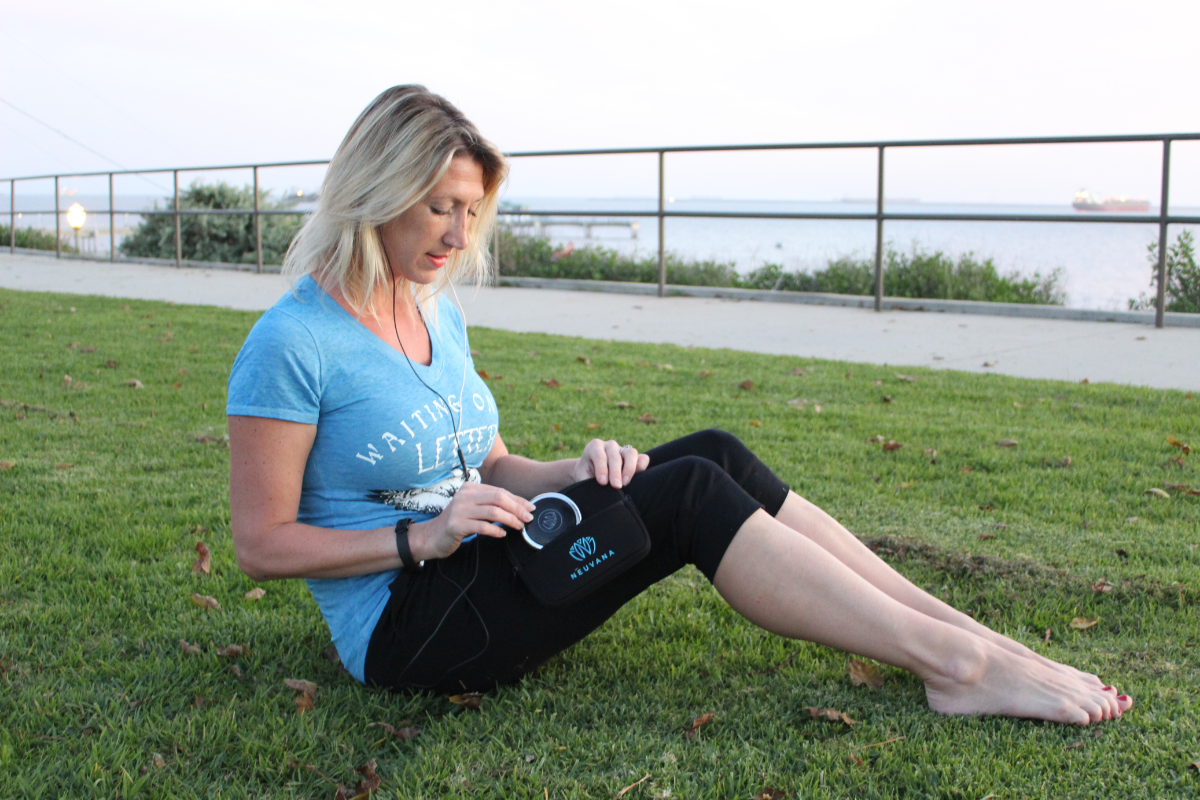 a woman sits in the grass using her xen by neuvana device