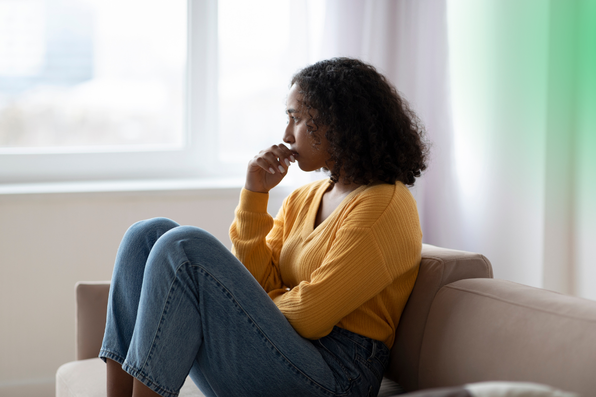 A woman in a yellow sweater sits looking out a window contemplating
