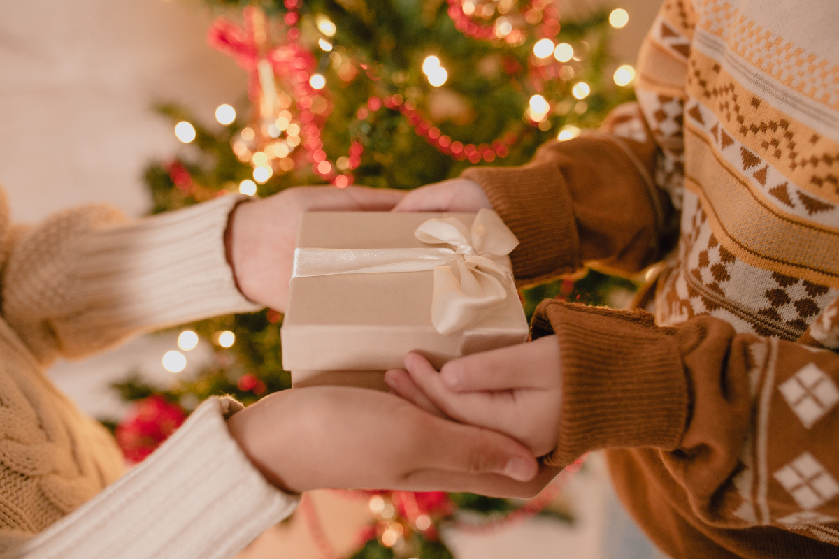 a pair of hands exchange a gift in front of a christmas tree