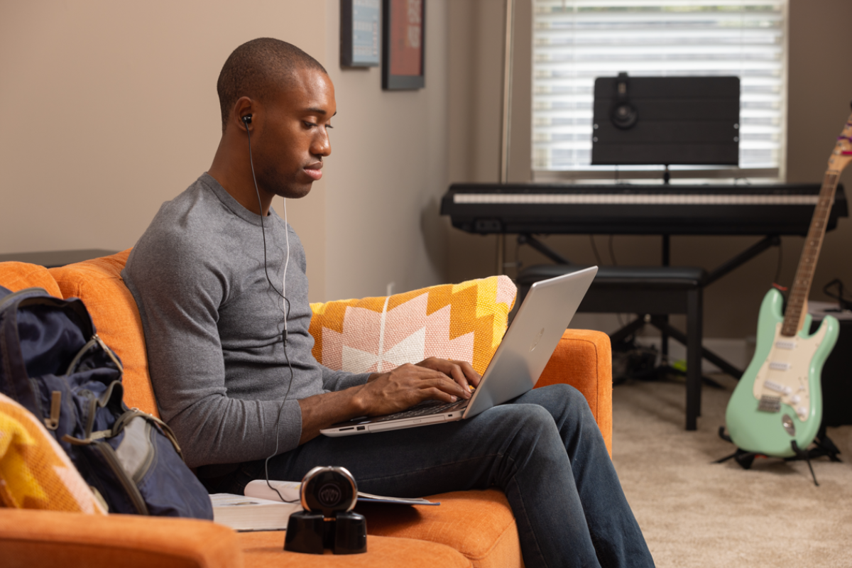 Men sitting on couch with laptop with the neuvana device on the table and the headphones in his ear