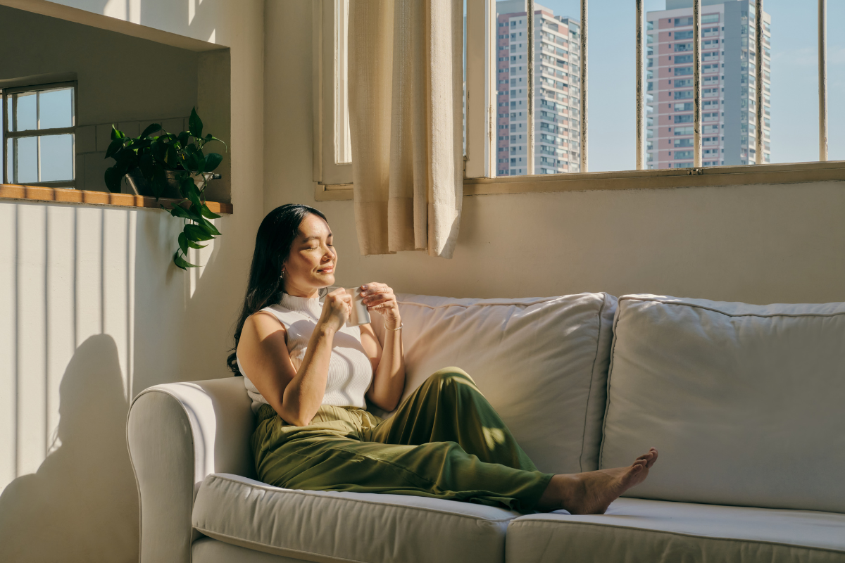a woman relaxing on a couch in front of a window sipping tea as the sun beams onto her