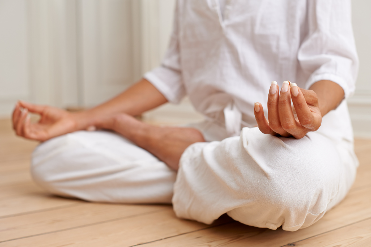 Image of a person dressed in all white sitting on the floor cross legged with their hands resting on their knees in a meditation pose