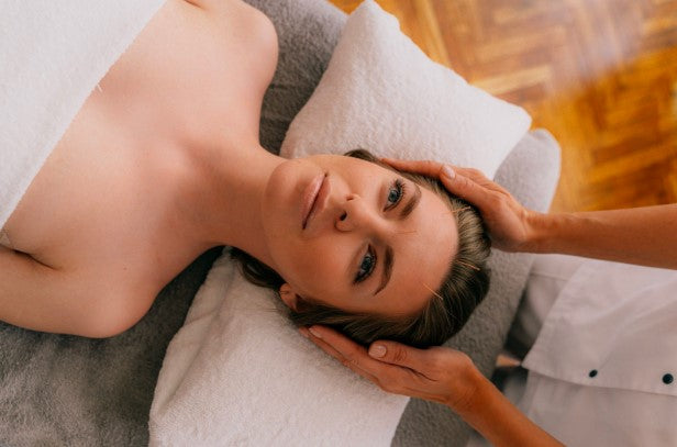 woman laying on spa treatment bed looking upwards, getting her head massaged