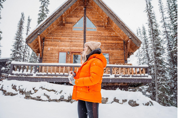 woman standing outside of cabin in the snow during holiday season