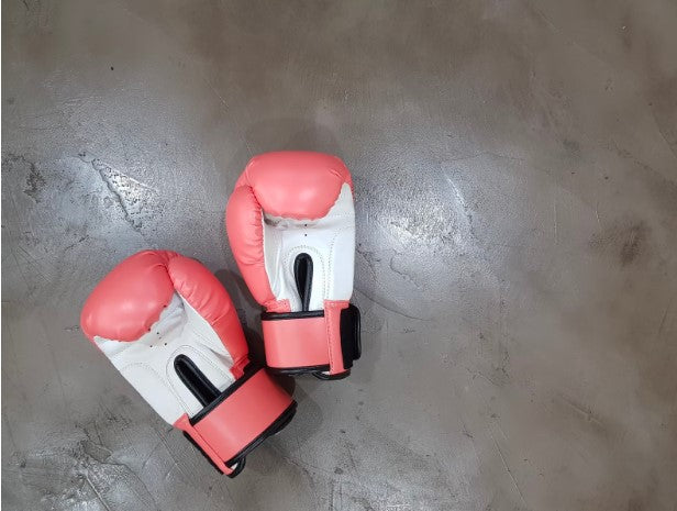 Bright red boxing gloves with white palms rest on a cement floor