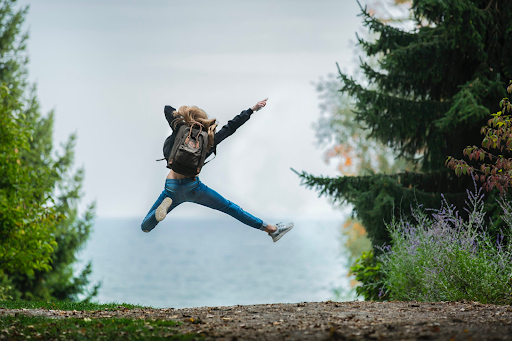girl jumping for joy in front of a beautiful lake outlined by pine trees