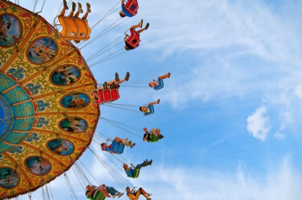 Colorful yellow and green amusement park swing juxtaposed by a stunning blue sky. People wearing colorful shades of red, blue, and yellow swing merrily through the air. 
