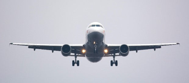 Grey commercial plane flying head on through a light grey sky 