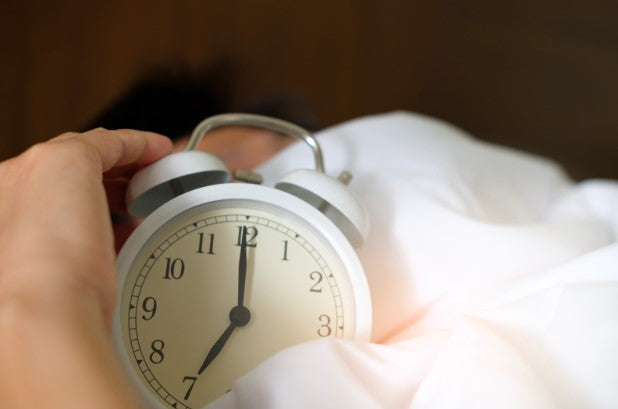 Person in bed clutches an old school alarm clock 